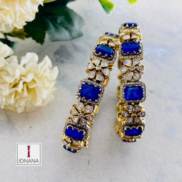 A PAIR OF GOLD PLATED BLUE DOUBLET MOISSANITE FLORAL BANGLES (2.4 OPENABLE)